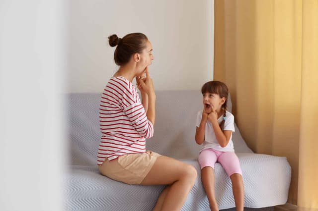 Fizjoterapeuta w pasiastej koszuli, pracujący nad wadami mowy lub trudnościami z małą dziewczynką w domu, siedząc na kanapie, prywatne lekcje poprawiające wymowę dźwięków. Dysleksja